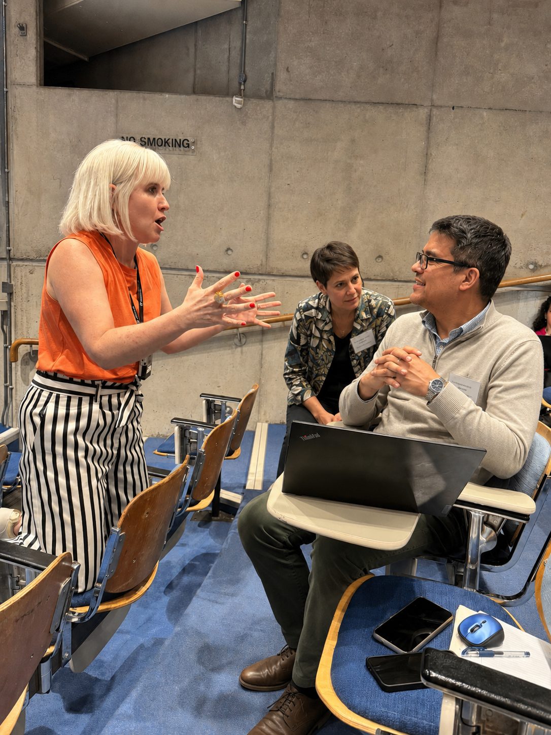 Brooke Gallagher leaning in to help a participant at their laptop during the Opera Europa AI literacy session, with other attendees working around the table.